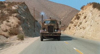 Movie still from “Duel” (1971), directed by Steven Spielberg – A truck driving down a road near a mountain; Extreme Wide shot, High angle