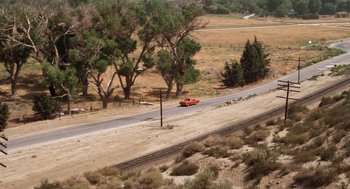 Movie still from “Duel” (1971), directed by Steven Spielberg – An orange car driving down a road next to a telephone pole; Extreme Wide shot, High angle