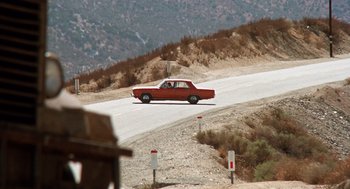 Movie still from “Duel” (1971), directed by Steven Spielberg – A red car driving down a road next to a hill; Extreme Wide shot, High angle