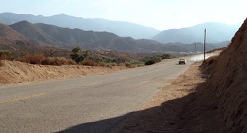 Movie still from “Duel” (1971), directed by Steven Spielberg – A car driving down a road in the middle of the desert; Extreme Wide shot, High angle
