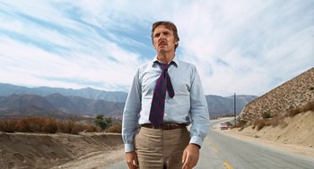 Movie still from “Duel” (1971), directed by Steven Spielberg – A man standing on the side of a road wearing a tie; Medium shot, Low angle
