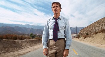 Movie still from “Duel” (1971), directed by Steven Spielberg – A man standing on the side of a road wearing a tie; Medium shot, Low angle
