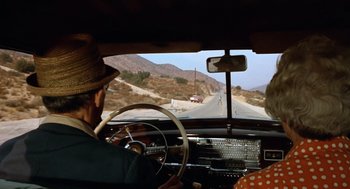 Movie still from “Duel” (1971), directed by Steven Spielberg – An older man driving a car on a road; Wide shot, High angle