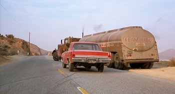 Movie still from “Duel” (1971), directed by Steven Spielberg – An old red car is driving behind a tanker truck on the side of the road; Wide shot, Low angle