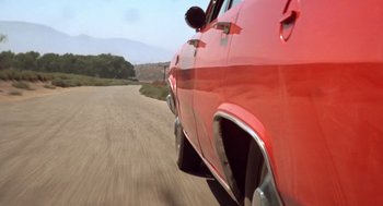 Movie still from “Duel” (1971), directed by Steven Spielberg – View of the side of a red car driving down the road; Wide shot, Low angle