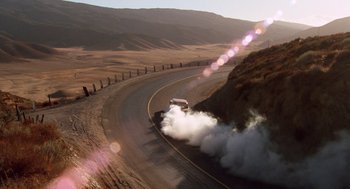 Movie still from “Duel” (1971), directed by Steven Spielberg – A car is driving down a road with smoke coming out of the exhaust; Extreme Wide shot, High angle