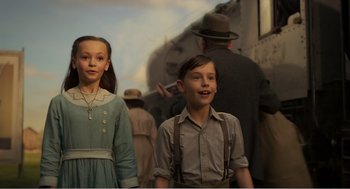 Movie still from “Dumbo” (2019), directed by Tim Burton – Two young people standing next to each other in front of a train; Medium shot, Low angle