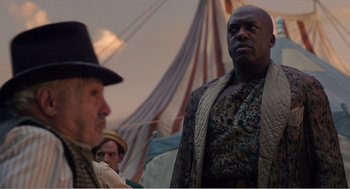 Movie still from “Dumbo” (2019), directed by Tim Burton – A man in a hat and a jacket standing next to another man in a hat; Medium shot, Over the shoulder angle