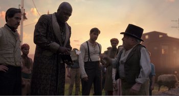 Movie still from “Dumbo” (2019), directed by Tim Burton – A group of men standing around in a field at sunset; Medium shot, Over the shoulder angle