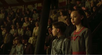 Movie still from “Dumbo” (2019), directed by Tim Burton – Two young people standing in front of an audience; Medium shot, High angle