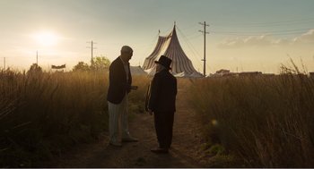 Movie still from “Dumbo” (2019), directed by Tim Burton – Two men standing on a dirt road in front of a tent; Wide shot, Low angle
