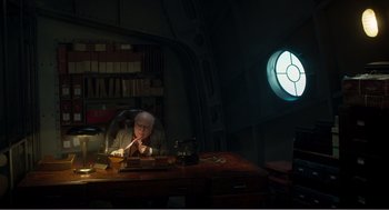 Movie still from “Dumbo” (2019), directed by Tim Burton – An older man sitting at a desk in a dark room; Wide shot, High angle