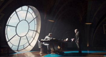 Movie still from “Dumbo” (2019), directed by Tim Burton – Two men sitting at a table in front of a clock; Wide shot, Low angle
