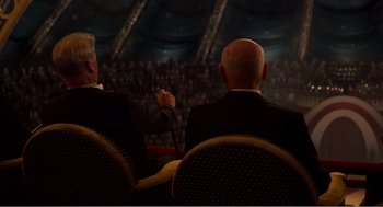 Movie still from “Dumbo” (2019), directed by Tim Burton – Two men are sitting in chairs and one of them is holding a microphone; Wide shot, Over the shoulder angle