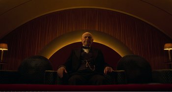 Movie still from “Dumbo” (2019), directed by Tim Burton – An old man sitting in a chair in a room; Medium shot, Low angle