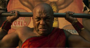 Movie still from “Dumbo” (2019), directed by Tim Burton – A man in a red and black shirt is lifting a bar; Close Up shot, Low angle