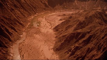 Movie still from “Dust Devil” (1992), directed by Richard Stanley – A view of a river running through a valley; Extreme Wide shot, High angle