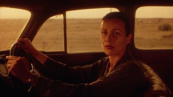 Movie still from “Dust Devil” (1992), directed by Richard Stanley – A woman sitting in the driver's seat of a car; Close Up shot, Low angle