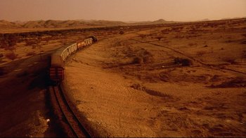 Movie still from “Dust Devil” (1992), directed by Richard Stanley – A train traveling down the tracks in the middle of the desert; Extreme Wide shot, Overhead angle