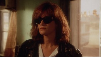 Movie still from “Dust Devil” (1992), directed by Richard Stanley – A person with sunglasses and long hair wearing a leather jacket; Close Up shot, Low angle