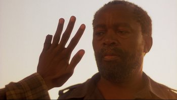 Movie still from “Dust Devil” (1992), directed by Richard Stanley – A person holding their hand up; Close Up shot, Low angle