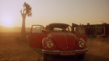 Movie still from “Dust Devil” (1992), directed by Richard Stanley – An old red vw beetle parked in a field; Wide shot, Low angle