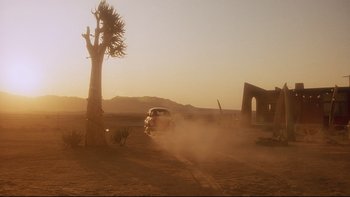 Movie still from “Dust Devil” (1992), directed by Richard Stanley – A car driving on a dirt road near a tree; Extreme Wide shot, Low angle