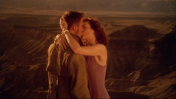 Movie still from “Dust Devil” (1992), directed by Richard Stanley – A man and a woman kissing in front of mountains; Medium shot, High angle
