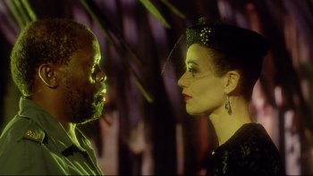 Movie still from “Dust Devil” (1992), directed by Richard Stanley – A man and a woman face to face in front of trees; Close Up shot, Low angle