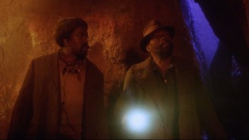 Movie still from “Dust Devil” (1992), directed by Richard Stanley – A couple of men standing next to each other in a cave; Medium shot, Low angle