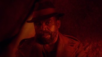 Movie still from “Dust Devil” (1992), directed by Richard Stanley – A man with a beard wearing a hat and a jacket; Close Up shot, Low angle