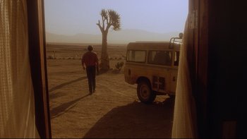 Movie still from “Dust Devil” (1992), directed by Richard Stanley – A man walking in the dirt near a tree; Wide shot, Low angle