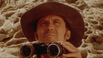 Movie still from “Dust Devil” (1992), directed by Richard Stanley – A man in a cowboy hat looking through binoculars; Close Up shot, Low angle