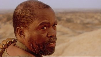 Movie still from “Dust Devil” (1992), directed by Richard Stanley – A person with a beard; Close Up shot, Over the shoulder angle