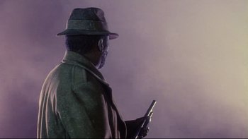 Movie still from “Dust Devil” (1992), directed by Richard Stanley – A man in a hat holding a cell phone in his hand; Close Up shot, Over the shoulder angle