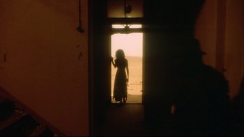 Movie still from “Dust Devil” (1992), directed by Richard Stanley – A woman standing at the door of a room; Wide shot, Over the shoulder angle