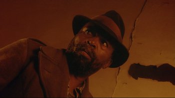 Movie still from “Dust Devil” (1992), directed by Richard Stanley – A man with a beard wearing a brown hat; Close Up shot, Low angle