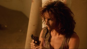 Movie still from “Dust Devil” (1992), directed by Richard Stanley – A woman holding a handgun while standing next to a pillar; Close Up shot, High angle