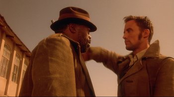 Movie still from “Dust Devil” (1992), directed by Richard Stanley – Two men are standing in a field touching each other's hair; Close Up shot, Over the shoulder angle