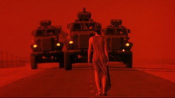 Movie still from “Dust Devil” (1992), directed by Richard Stanley – A woman standing in the middle of the road in front of a line of military vehicles; Wide shot, Low angle