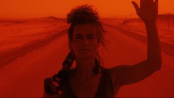 Movie still from “Dust Devil” (1992), directed by Richard Stanley – A woman holding a gun while standing on the side of a road; Close Up shot, Low angle