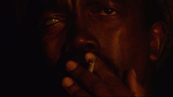 Movie still from “Dust Devil” (1992), directed by Richard Stanley – A man is smoking a cigarette in the dark; Extreme Close Up shot, Low angle