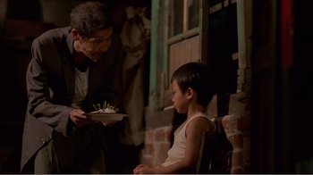 Movie still from “Dust in the Wind” (1986), directed by Hsiao-Hsien Hou – A man and a boy are holding a plate of food in front of a window; Medium shot, Over the shoulder angle