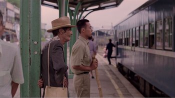 Movie still from “Dust in the Wind” (1986), directed by Hsiao-Hsien Hou – A man standing next to another man on a train platform; Medium shot, Over the shoulder angle