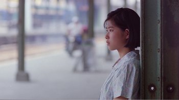 Movie still from “Dust in the Wind” (1986), directed by Hsiao-Hsien Hou – A young woman standing on the sidewalk looking off into the distance; Close Up shot, Over the shoulder angle
