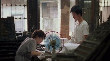 Movie still from “Dust in the Wind” (1986), directed by Hsiao-Hsien Hou – Two people working on a piece of art in a room; Medium shot, Over the shoulder angle