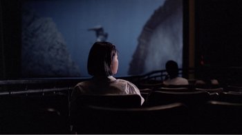 Movie still from “Dust in the Wind” (1986), directed by Hsiao-Hsien Hou – Two people sitting in front of a projection screen at night; Extreme Wide shot, Over the shoulder angle