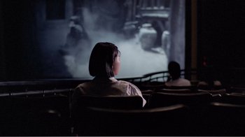Movie still from “Dust in the Wind” (1986), directed by Hsiao-Hsien Hou – Two people sitting in front of a projector screen; Wide shot, Over the shoulder angle