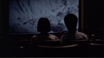 Movie still from “Dust in the Wind” (1986), directed by Hsiao-Hsien Hou – Two people sitting in front of a television screen; Medium shot, High angle