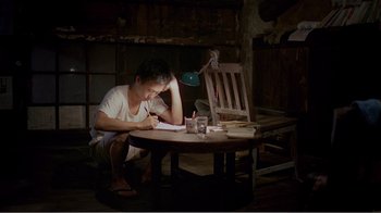 Movie still from “Dust in the Wind” (1986), directed by Hsiao-Hsien Hou – A man sitting at a table writing on a piece of paper; Wide shot, High angle